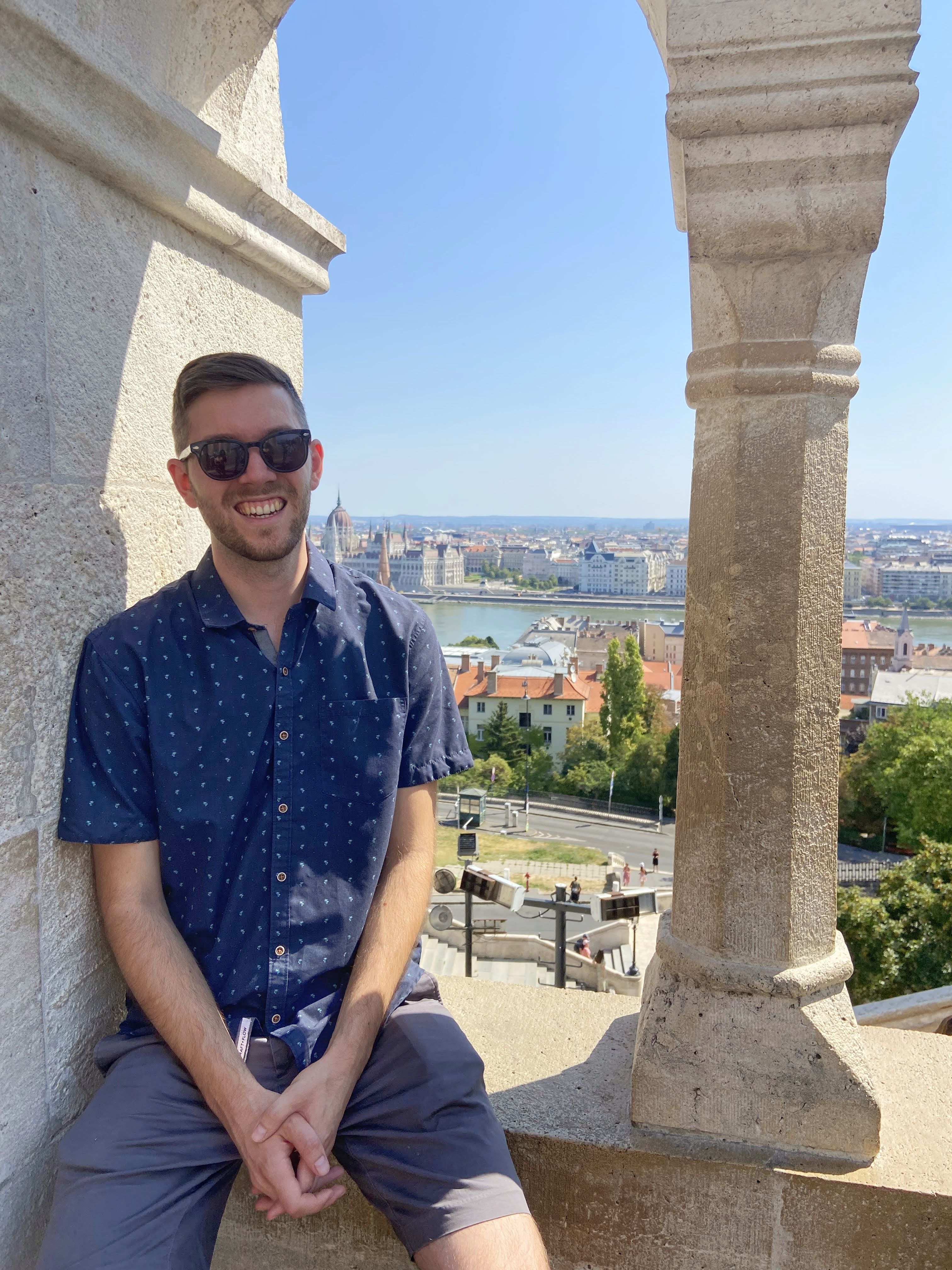 A man sitting on a ledge overlooking a European city along a river